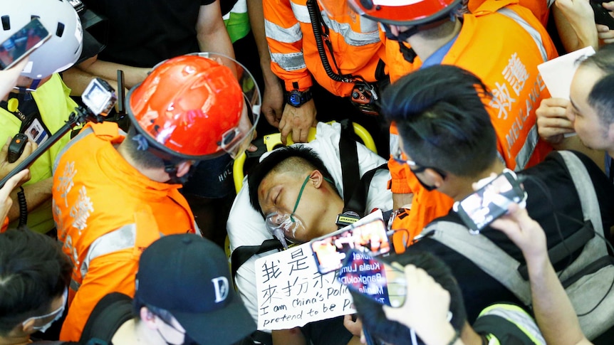 A man on a stretcher with his eyes closed surrounded by medics in orange vests and helmets