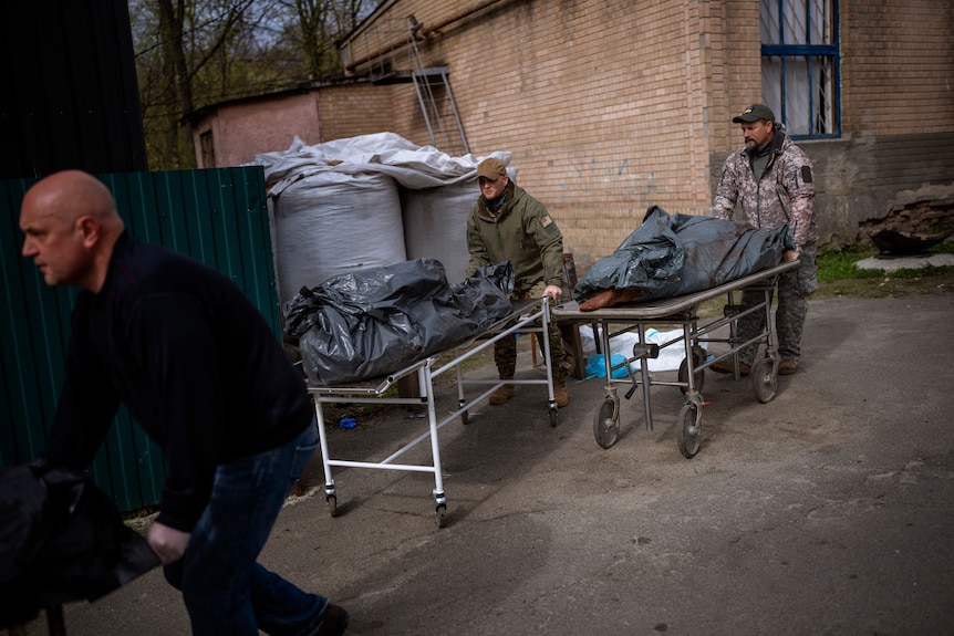 Volunteers move bodies wrapped in plastic from trucks.