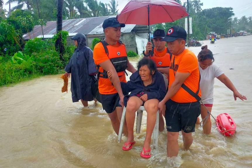 rescuers carry a woman in a plastic chair through flood waters as other people walk through water near by