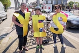 Two women and a young boy hold big gold letters spelling "YES" at an intersection.
