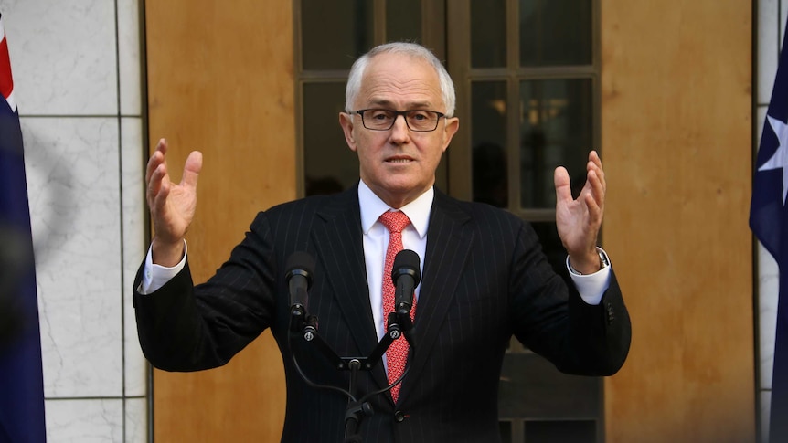 Malcolm Turnbull speaks in front of microphones with his hands in the air