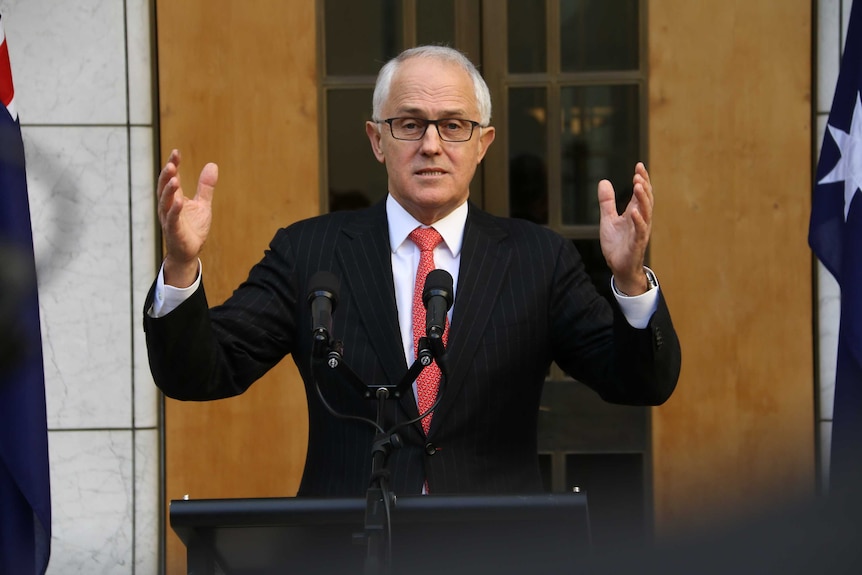 Malcolm Turnbull speaks in front of microphones with his hands in the air
