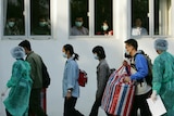 A group of masked Chinese people walk past windows, from which masked people watch them 