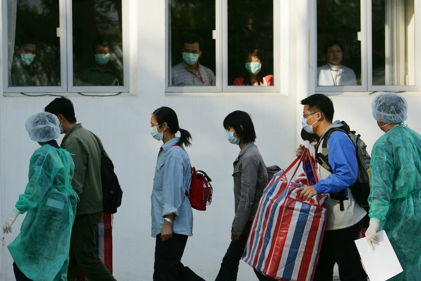 一群蒙面中国人走在蒙面人看到他们的窗户前 