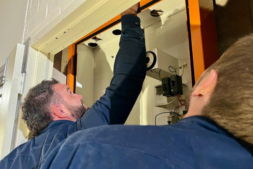 Two men work on a fuse box.
