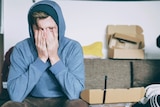 A man in a blue long sleeve shirt with his hands on his face sitting on a couch