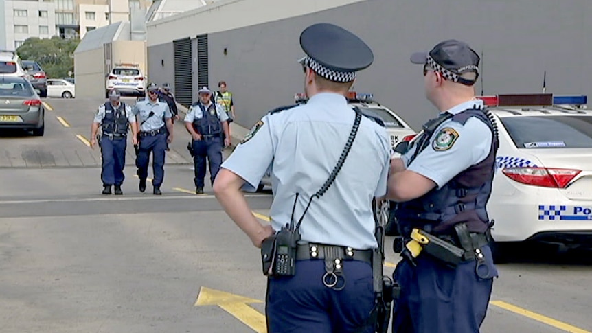 Police walking and standing at the site of a shooting in a Bankstown shopping centre car park.