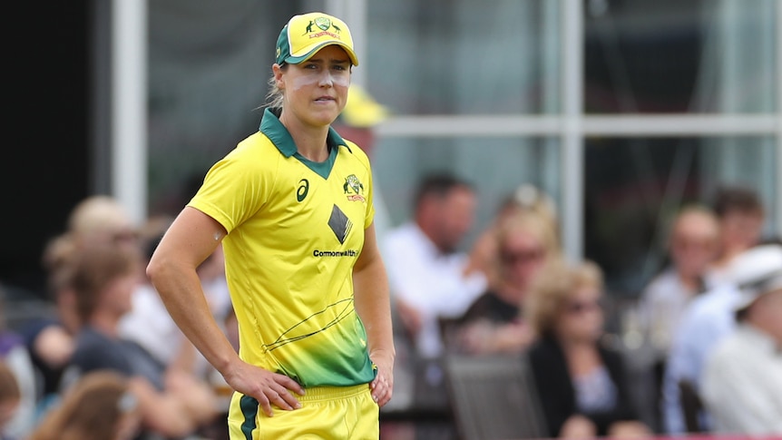 Ellyse Perry stands with her hands on her hips in yellow cricket kit