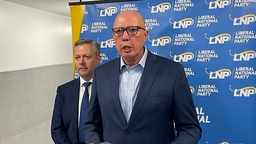 A man speaking to the press with another man behind him in front of a Liberal Party banner.