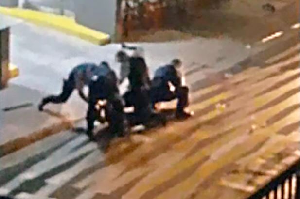 Several police officers crouch around a teenager on the ground, with one officer raising his baton above his head.