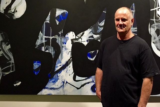 Chris Hopewell stands besides a large painting.