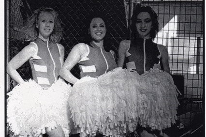 Black and white picture from a newspaper of three young women holding white pom-poms