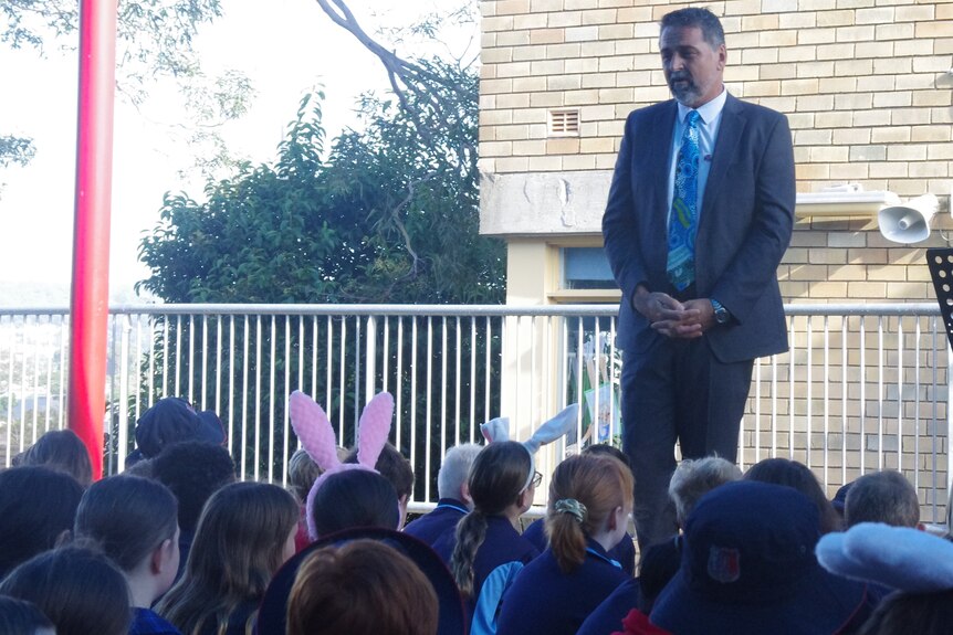 A school principal speaks to his students at an outdoor school assembly.