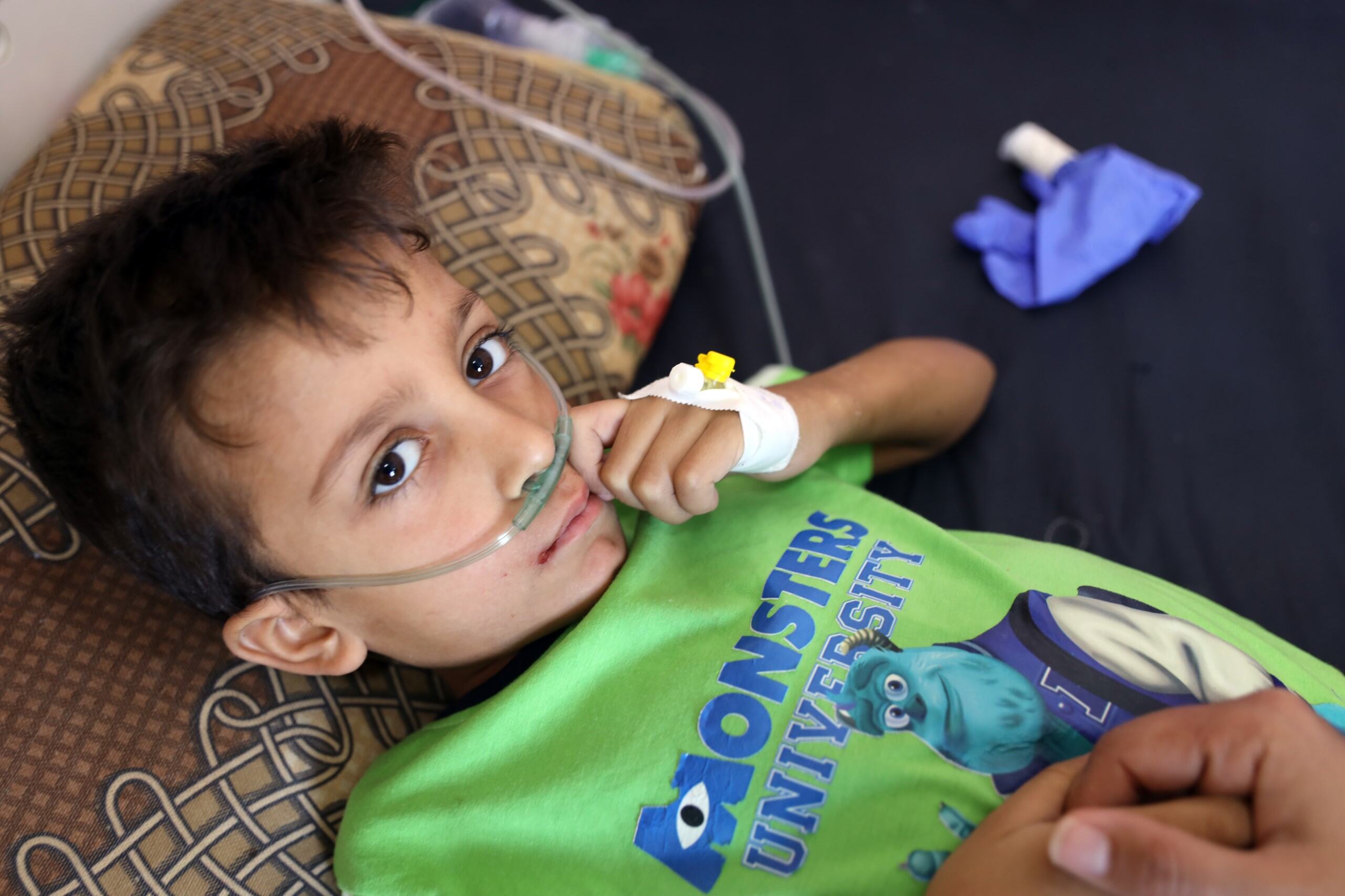 A sick boy looks up at the camera from his hospital bed 
