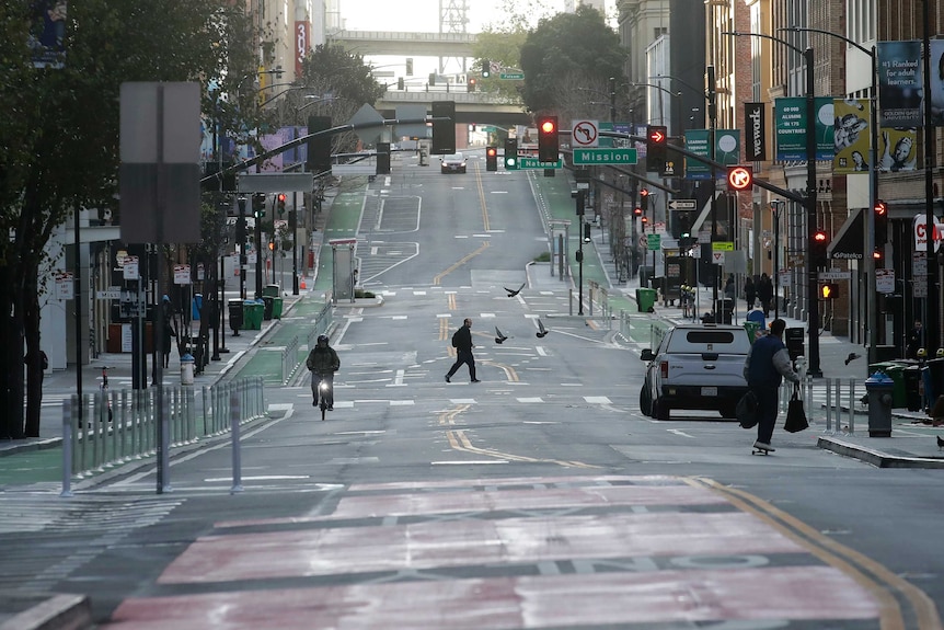 A man crosses a nearly empty street in San Francisco as another rides past on a bike.