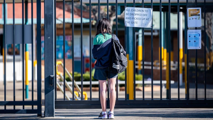 a young girl standing at the gates of an empty school