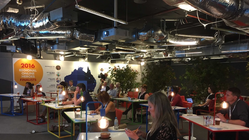 People sit at different coloured desks in large room at Google office at Pyrmont, Sydney