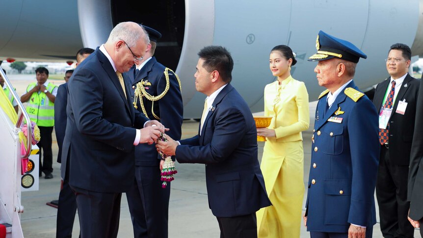 On the tarmac, Scott Morrison is greeted by Thailand's Varawut Silpa-archa who places a gift in Mr Morrison's hands.