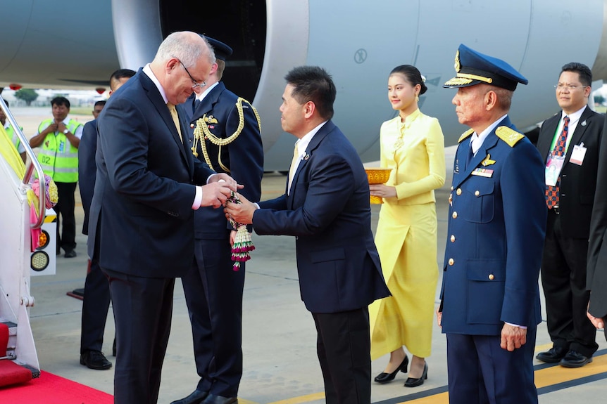 On the tarmac, Scott Morrison is greeted by Thailand's Varawut Silpa-archa who places a gift in Mr Morrison's hands.