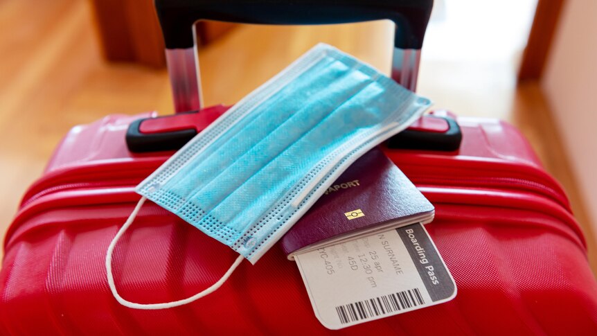 A mask and passport sit on top of a suitcase