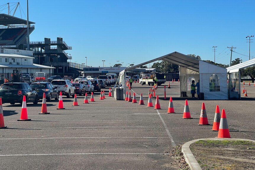 A testing site with a tent and traffic cones outside a sports stadium. Cars are lined up waiting for occupants to be tested