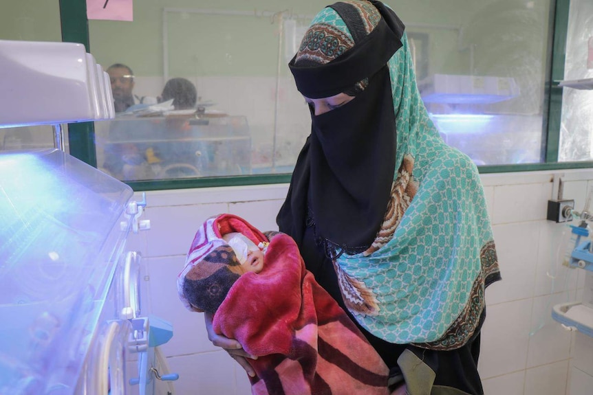 A woman wearing a nijab holds a newborn baby with eye patches