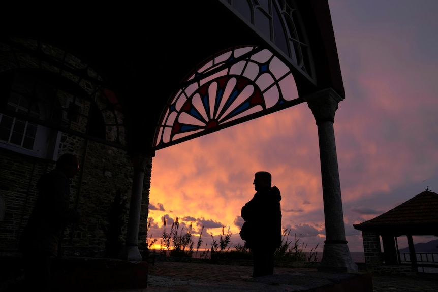 A man stands under an arch as the sun rises. 