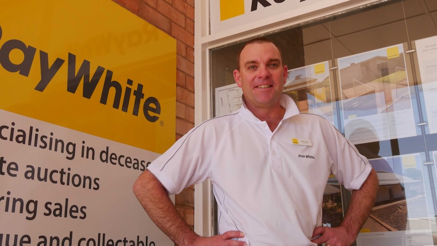 Real estate agent smiles with hands on hips in front of Ray White signs