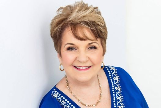 A smiling woman with a colourful top and golden jewellery.