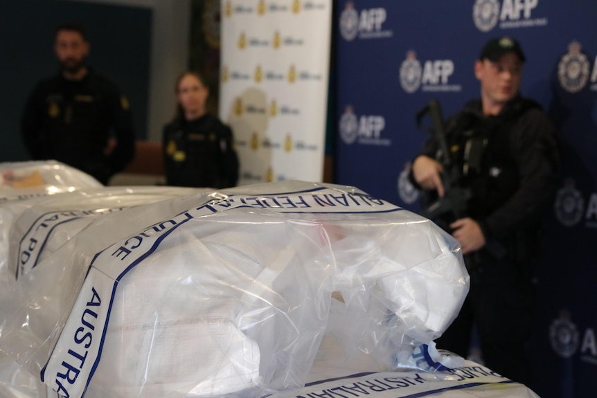 A close-up shot of plastic bags filled with cocaine with police officers in the background.