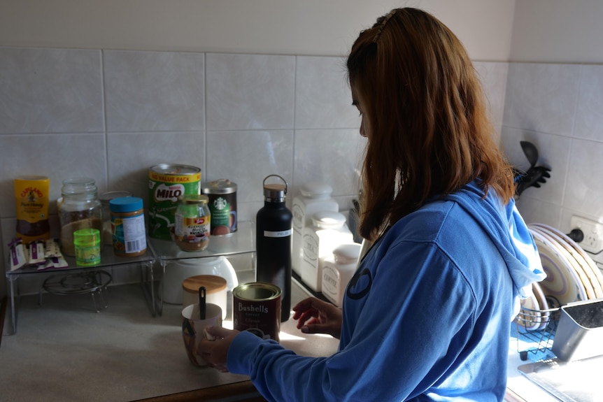 A woman stands in a kitchen making a coffee. 