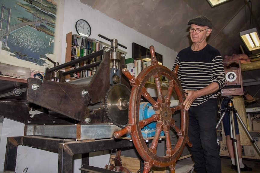 A man turning the ship's wheel handle of a printing press machine