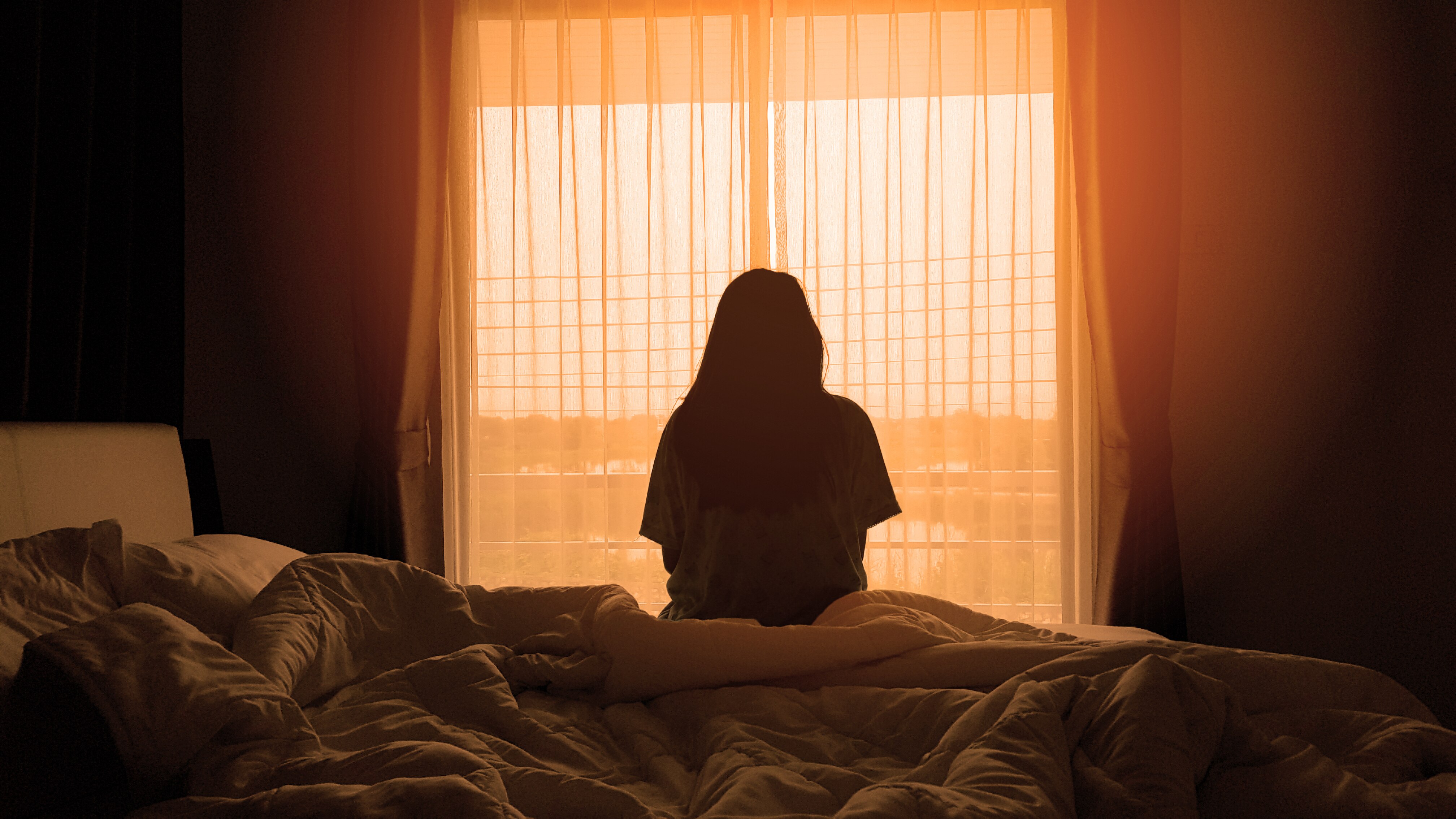 Silhouette of woman sitting on bed facing window.