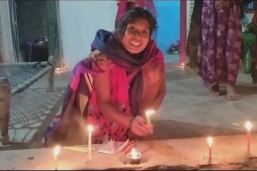 A women wearing pink and smilling kneeling on the floor and lighting candles