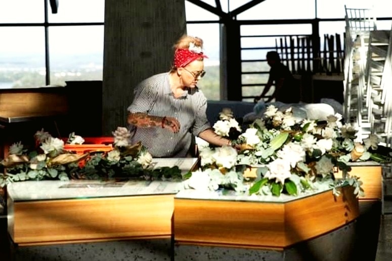 A lady with a red head scarf arranging flowers on a table.