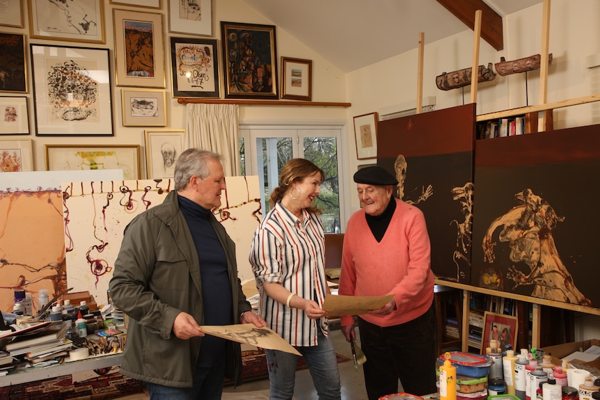 Three people stand in a busy art studio