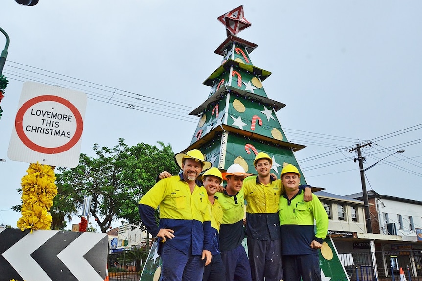 Five council workers in high viz standing in front of a large, green metal Christmas tree covered in road sign decorations