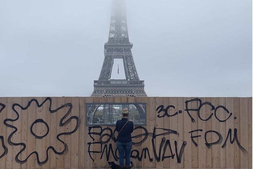 A woman looks at the Eiffel Tower through the hole in a fence.