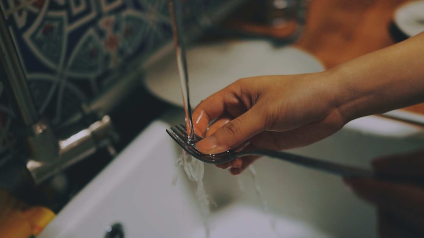 Woman rinsing a fork in the sink before stacking her dishes into the dishwasher