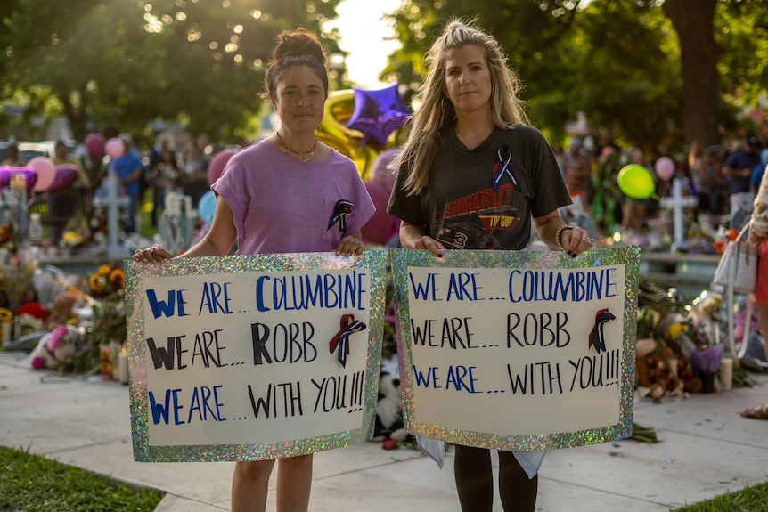 Two woman hold up signs that say "We are ... Columbine. We are ... Robb. We are with you."