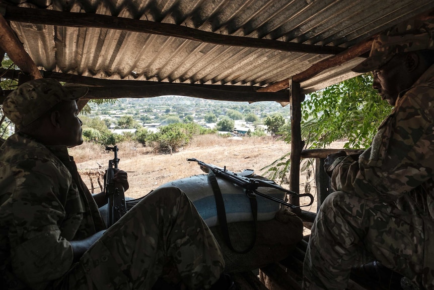 From inside a makeshift tin shed, you look from behind two armed Ethiopian soldiers sitting and looking out over a village.