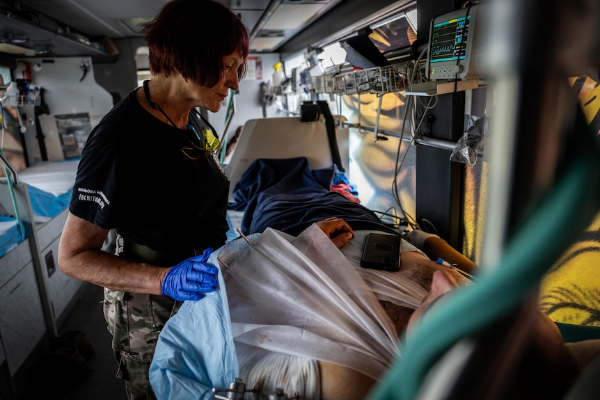 A woman with blue surgical glove rests a hand on a patient in a hospi