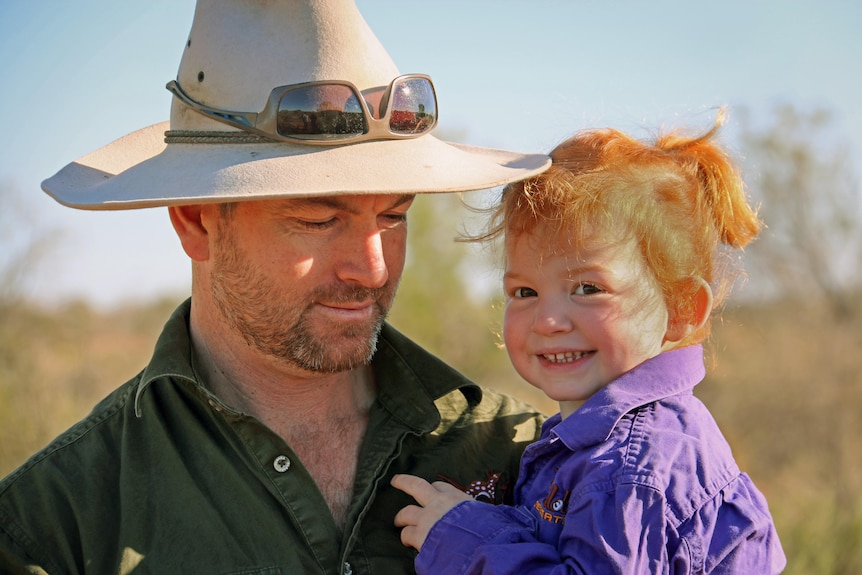 A man wearing a wide brim hat holds his young daughter