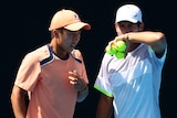 Two Australian male tennis players speak on court during a doubles match at the Australian Open.