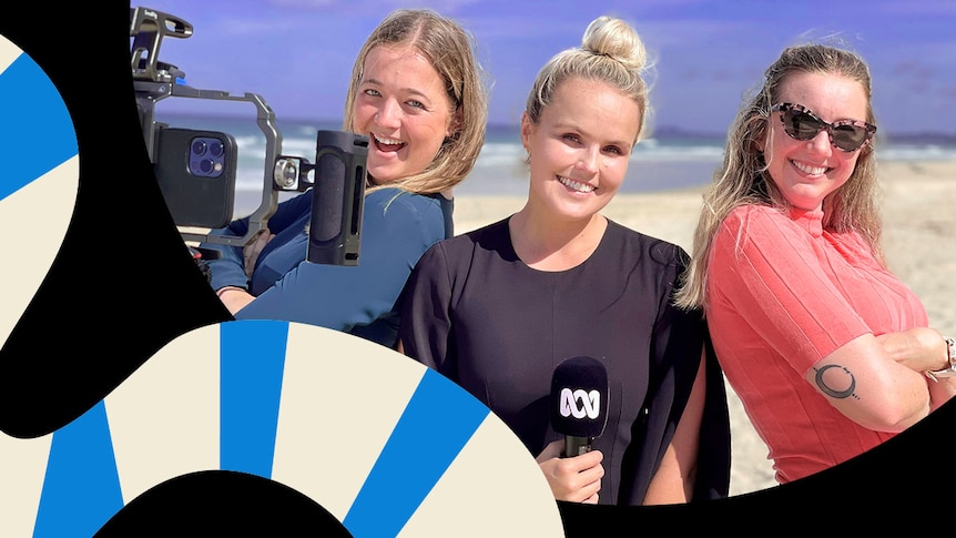 Three young woman smiling on a beach looking at the camera. One of them is holding an ABC microphone.