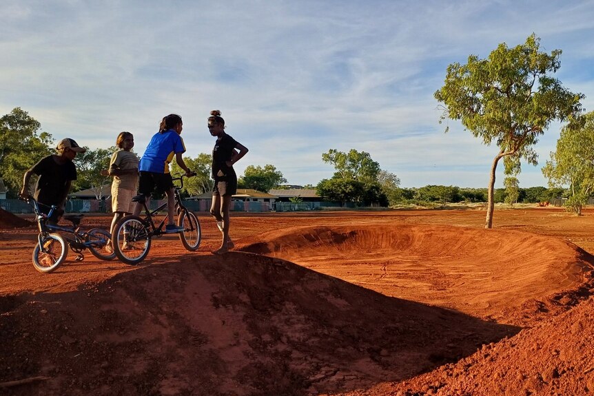 a group of children at the top of a jump on a dusty BMX track