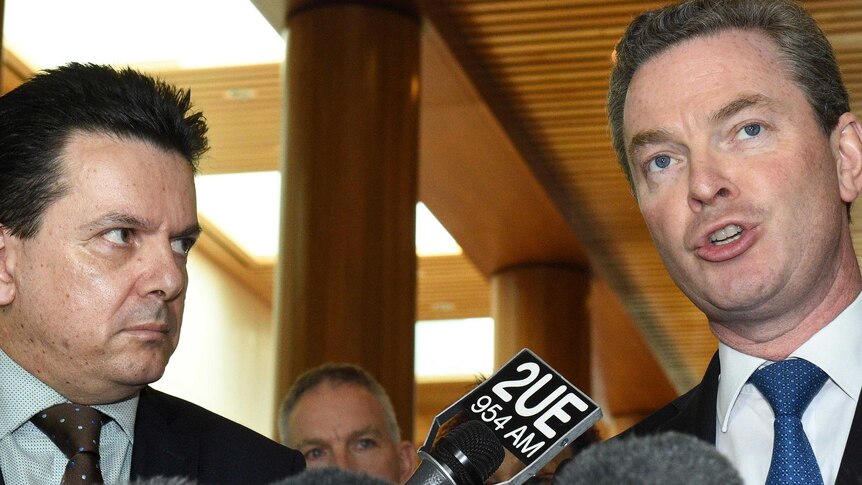 LtoR Nick Xenophon stares intently at Christopher Pyne as Mr Pyne speaks at a press conference.