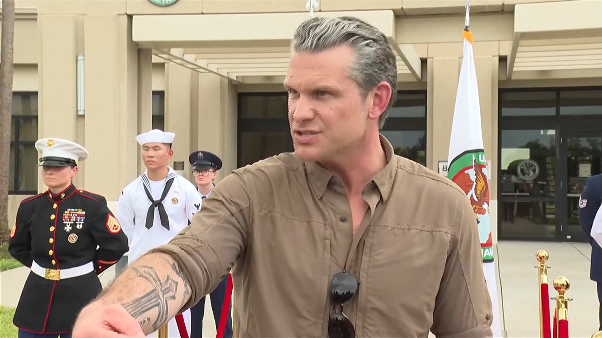 US Defense Secretary Pete Hegseth flanked by military personnel at an outdoor press conference.