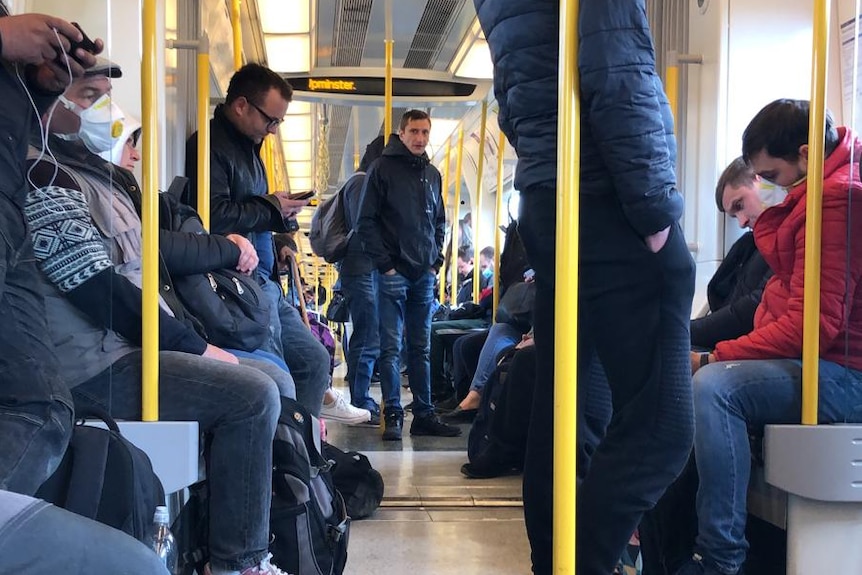 People stand and sit down on a train.