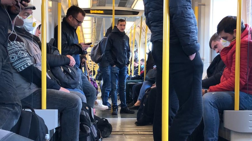 People stand and sit down on a train.